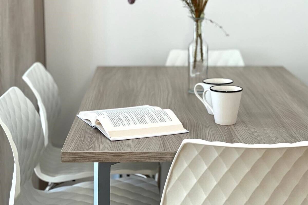 A dining table with a book, two mugs, and a vase with dried flowers.