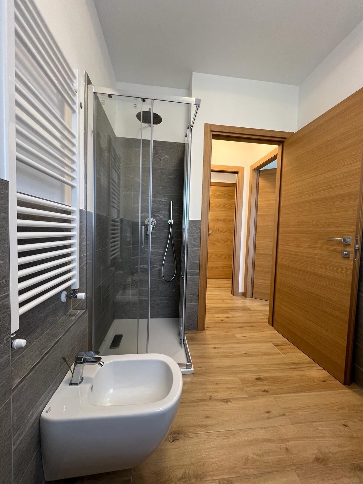 A modern bathroom with a glass-enclosed shower, a white bidet, and wooden flooring.