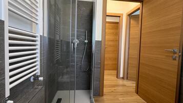 A modern bathroom with a glass-enclosed shower, a white bidet, and wooden flooring.