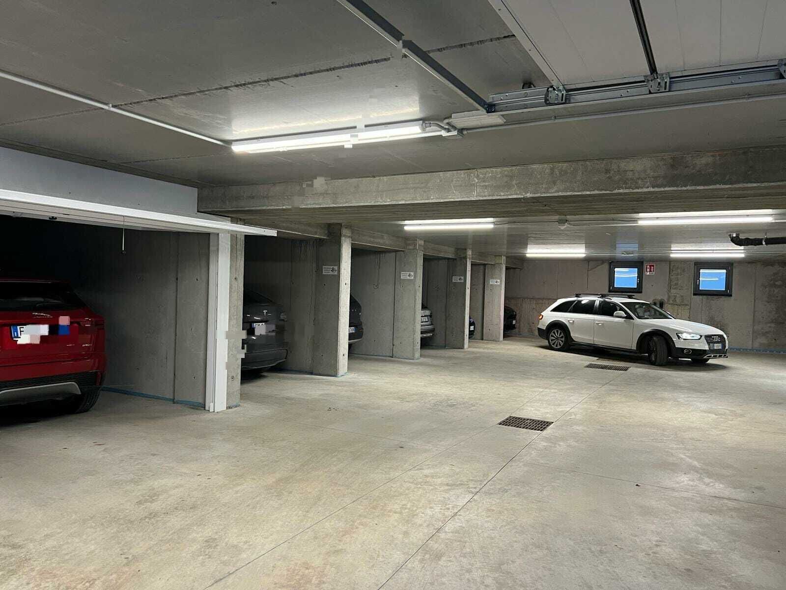 A multi-level parking garage with concrete pillars, overhead lighting, and a few cars parked.
