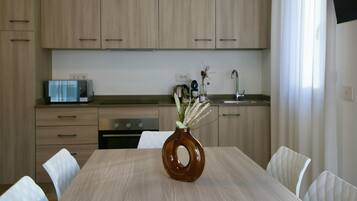 A modern kitchen with wooden cabinets, a dining table with chairs, and a vase with flowers on the table.