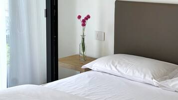 Ein Hotelzimmer mit einem Bett, einem Nachttisch, einer Blumenvase und einem Fenster mit Vorhängen.