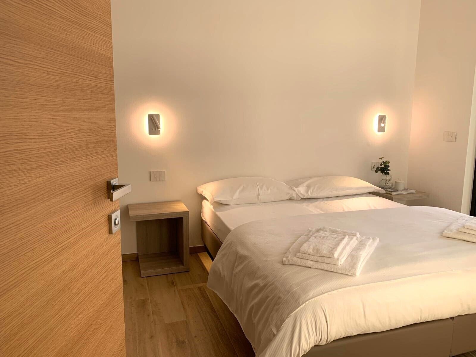 A bedroom with a bed, bedside tables, and wall-mounted lights.