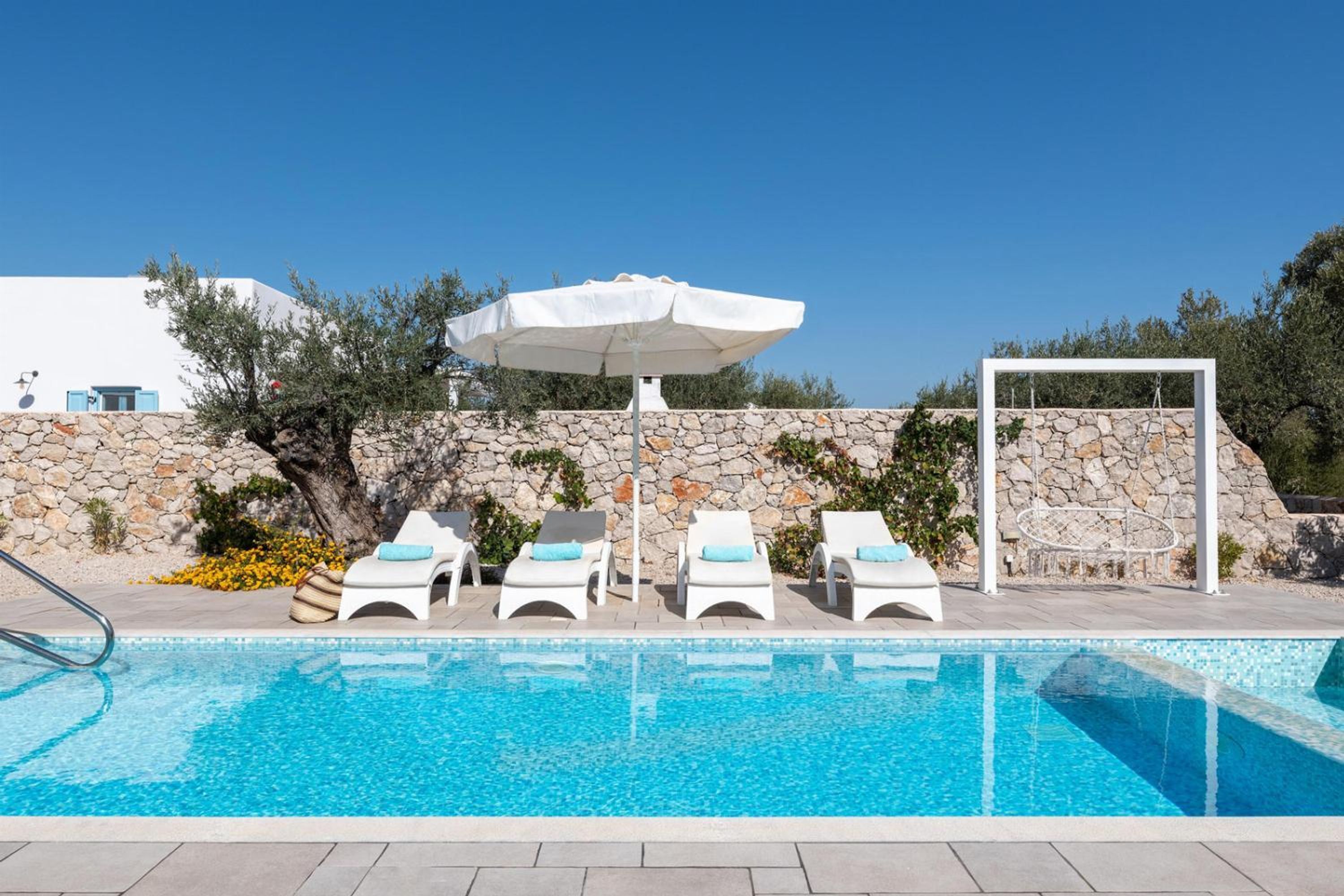 Una piscina blava i cristal·lina amb gandules blanques i un parasol blanc.