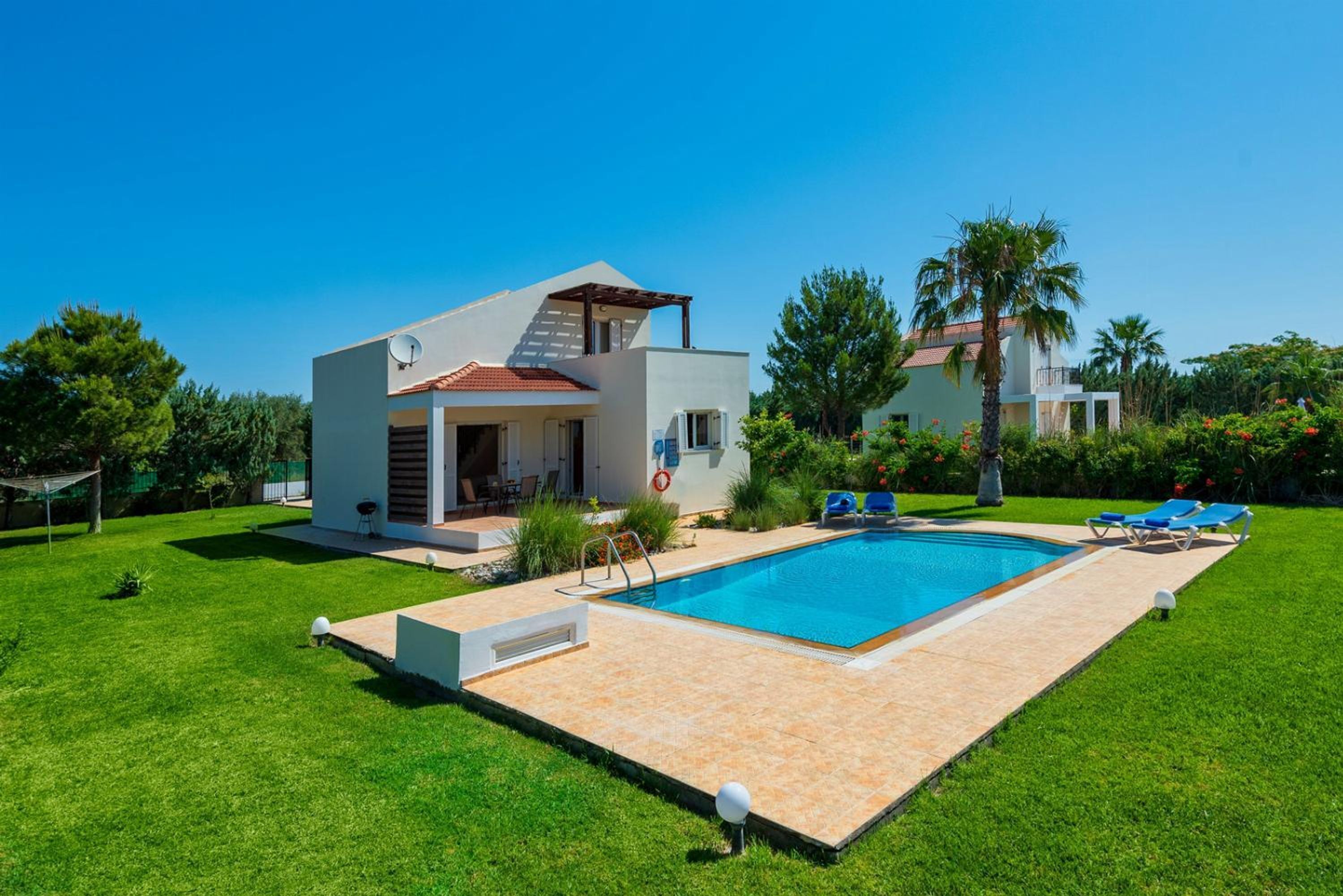 Una casa moderna de dos pisos con piscina, rodeada de césped cuidado y palmeras.