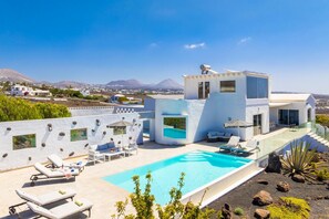 A modern villa with a swimming pool, lounge chairs, and a view of the landscape.