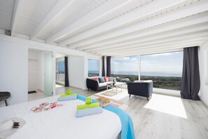A modern hotel room with a large bed, a sofa, a small table, and a view of the landscape.