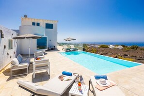 A poolside area with lounge chairs, a small table with a bottle, and a view of the sea. - The View in T as With 4 Bedrooms and 4 Bathrooms (Tías)