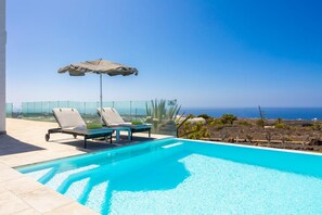 A swimming pool with lounge chairs and an umbrella, overlooking a coastal landscape. - The View in T as With 4 Bedrooms and 4 Bathrooms (Tías)