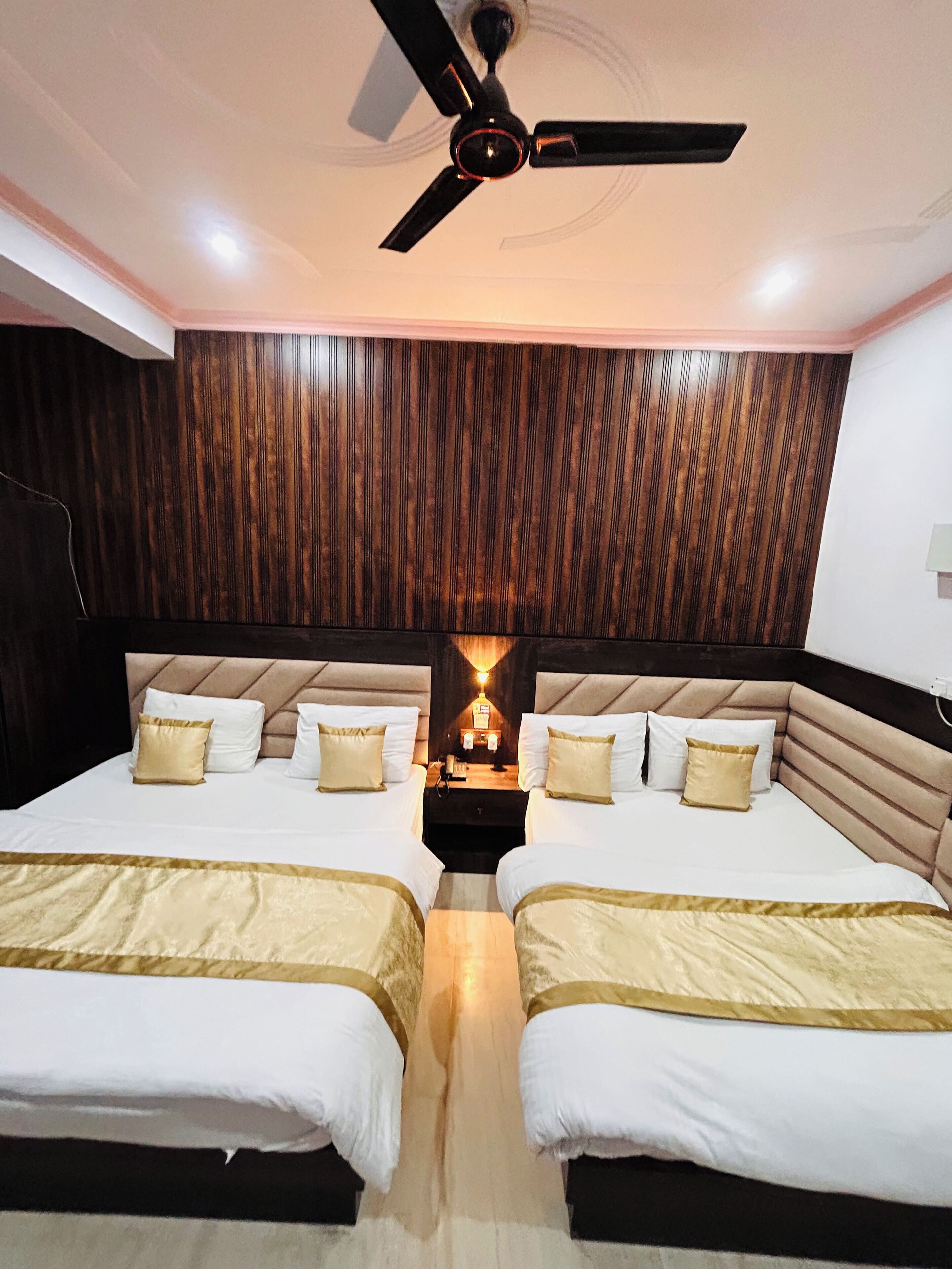 A hotel room with two beds, a ceiling fan, and a wooden wall panel.