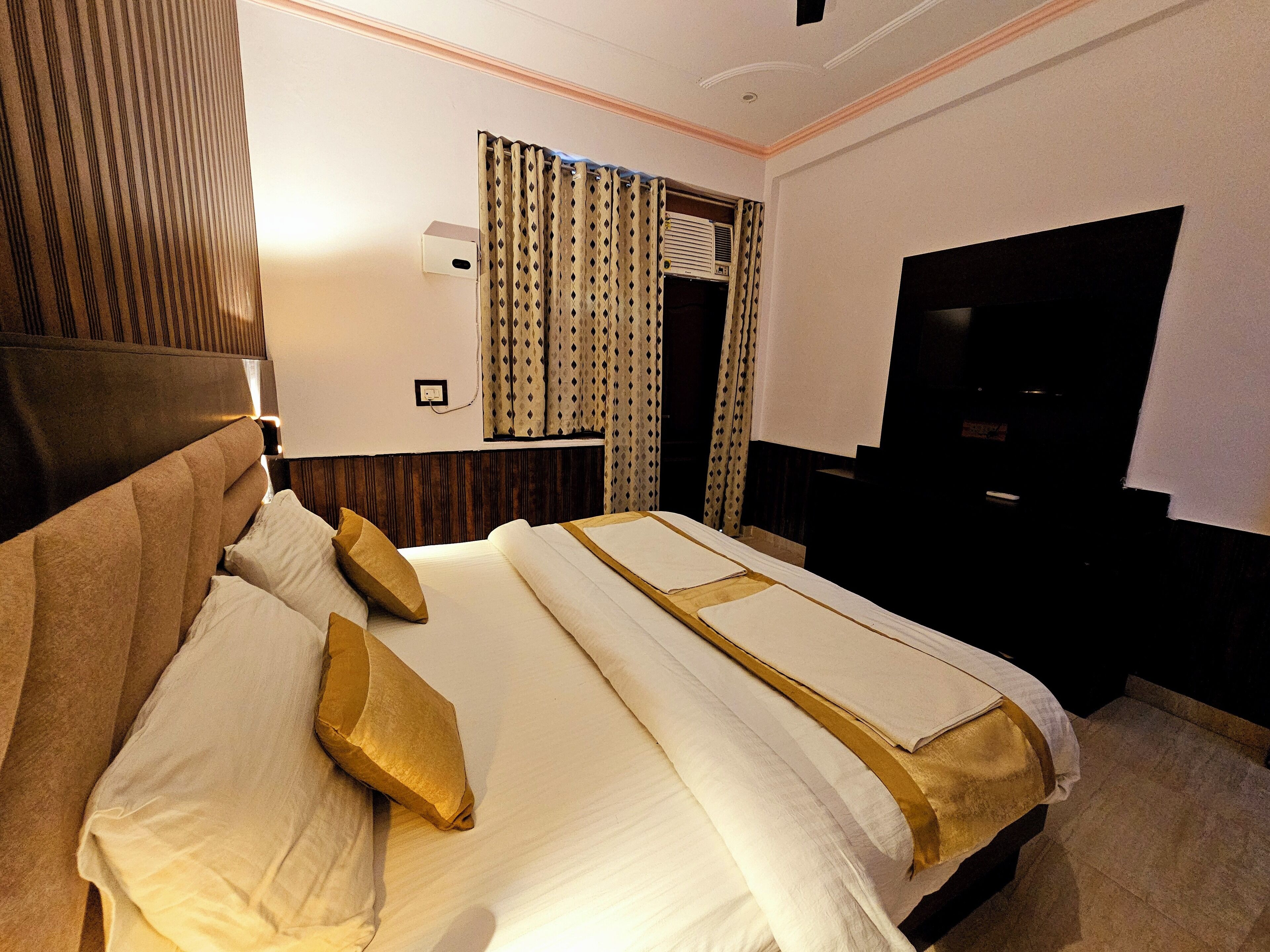A hotel room with a large bed, a flat-screen TV, and a window with patterned curtains.
