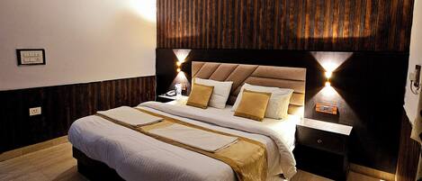 A modern bedroom with a large bed, wooden panel wall, ceiling fan, bedside lamps, and a nightstand.