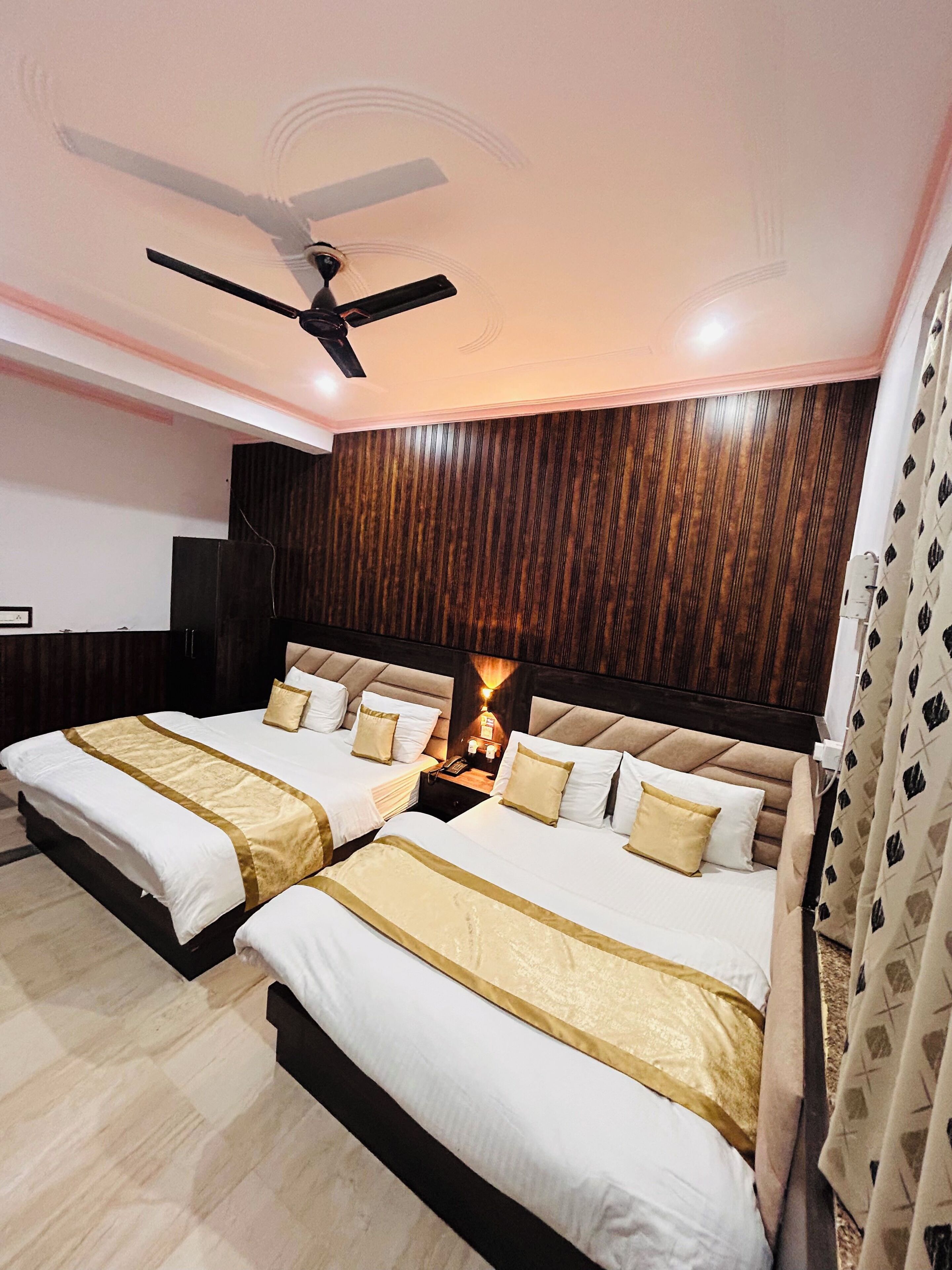 A hotel room with two beds, a ceiling fan, a wooden panel wall, and a nightstand with a lamp.