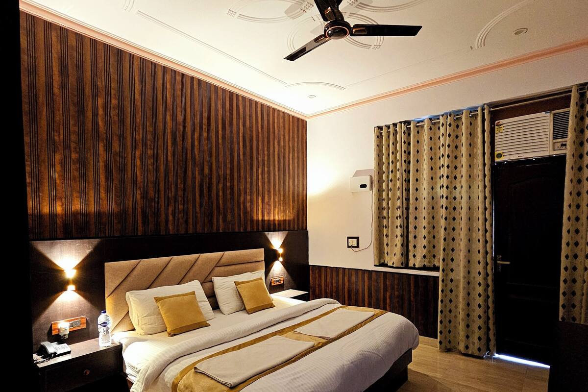A modern hotel room with a large bed, wooden paneling on the walls, a ceiling fan, and a nightstand with a lamp and a phone.