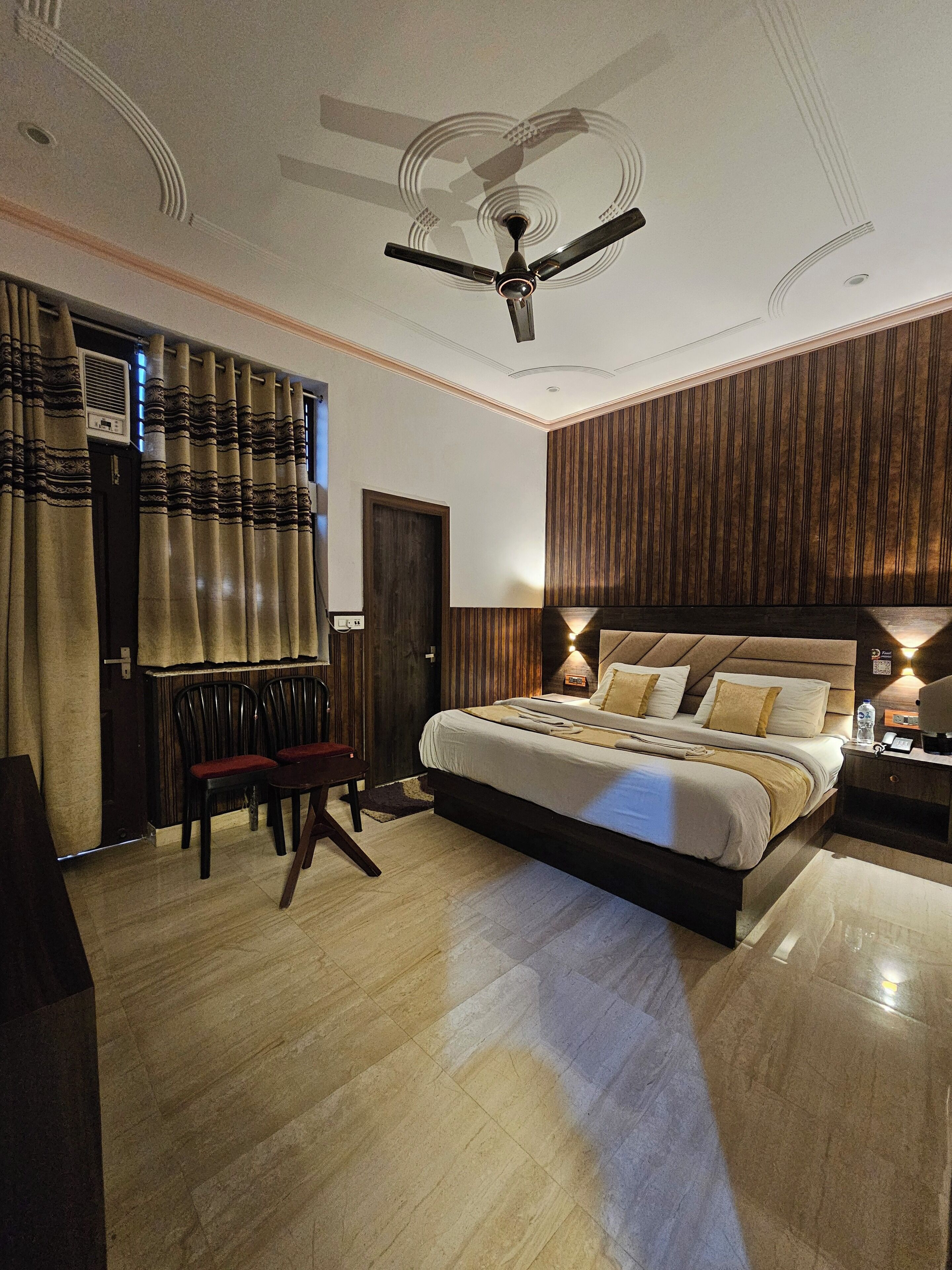 A modern bedroom with a large bed, a ceiling fan, and a wooden panel wall.