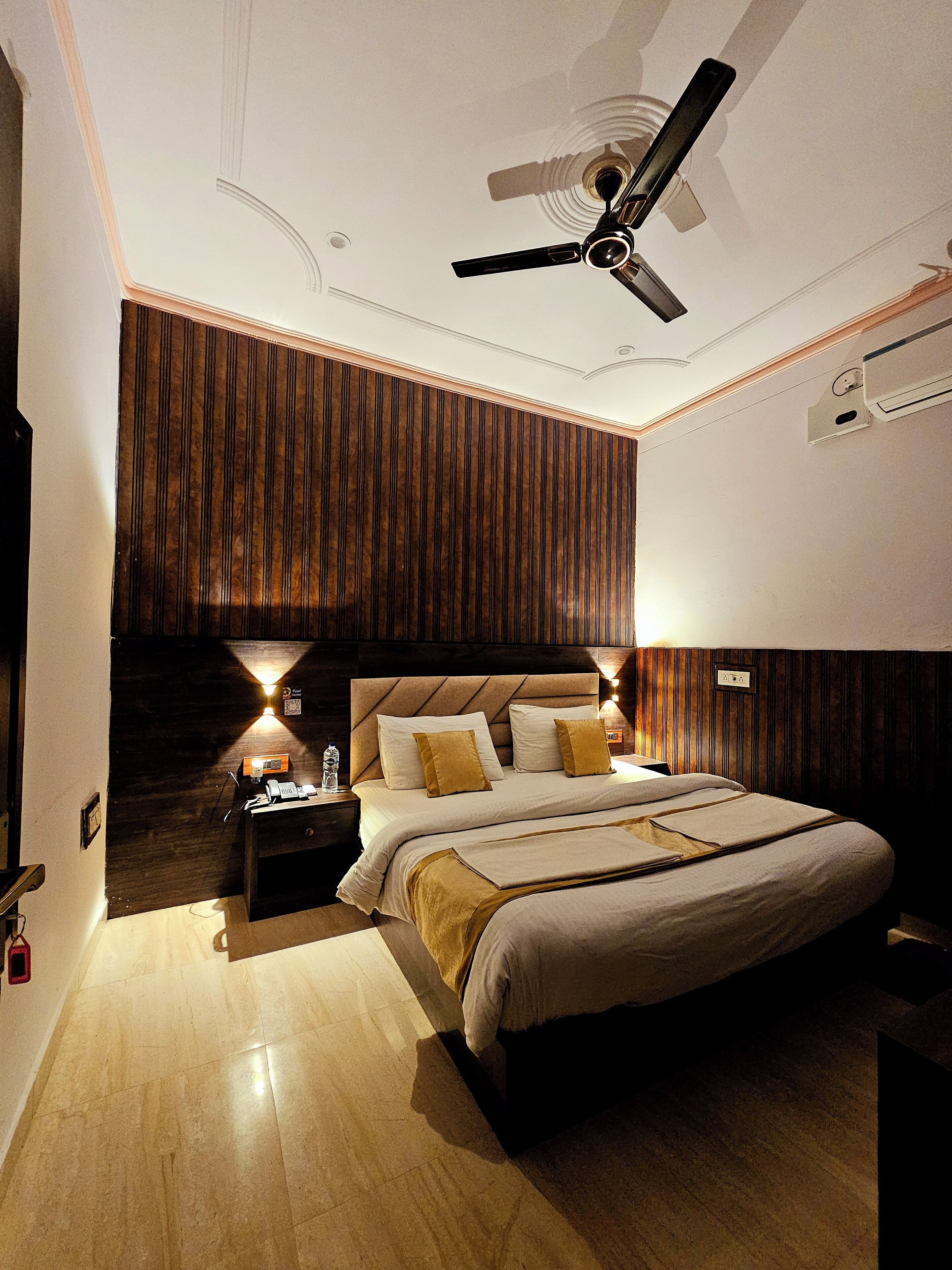 Un dormitorio con una cama grande, un ventilador de techo, una mesita de noche y un aire acondicionado instalado en la pared.