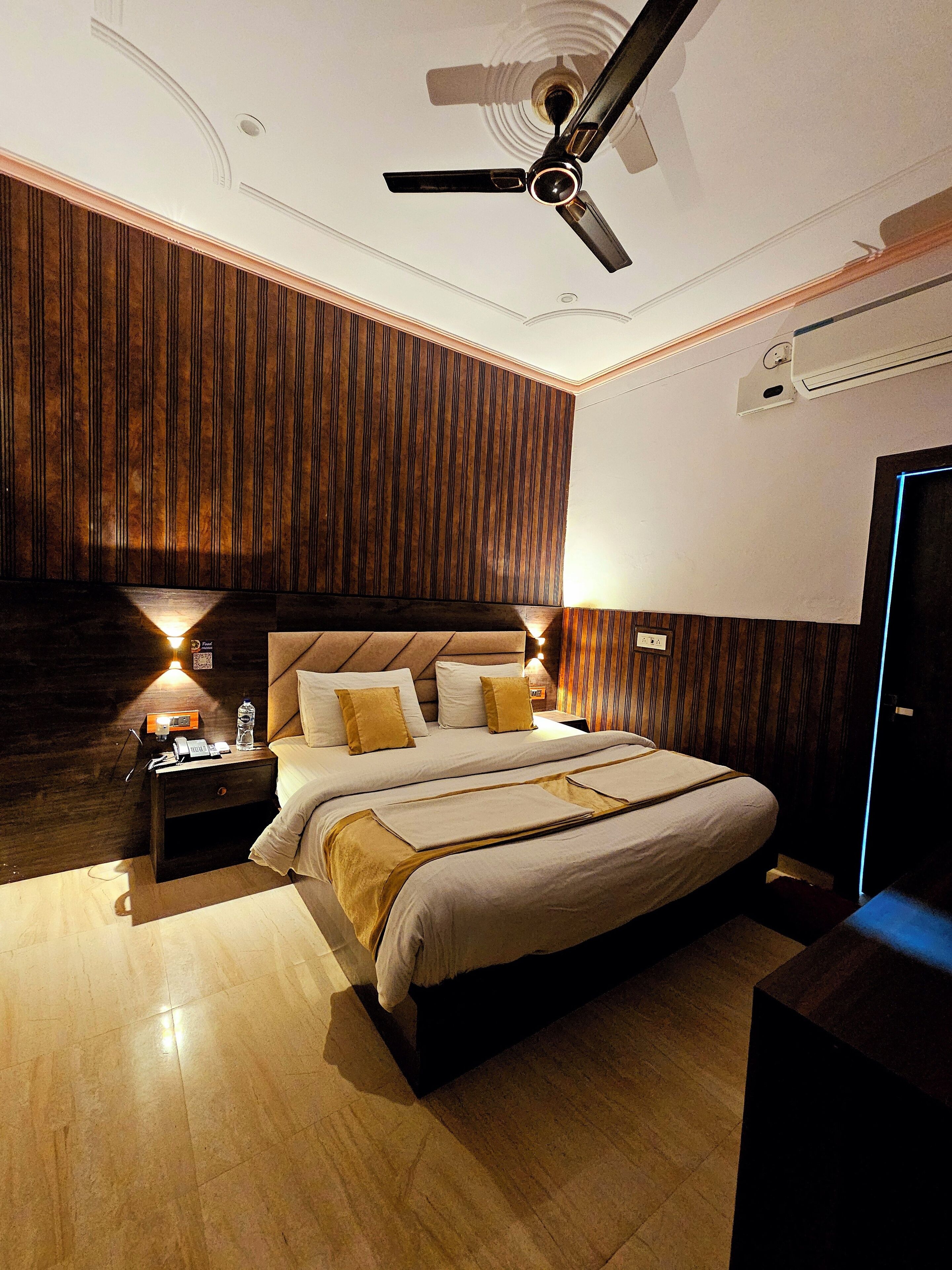 Un dormitorio moderno con una cama grande, paneles de madera en las paredes, un ventilador de techo y una mesita de noche con lámpara.