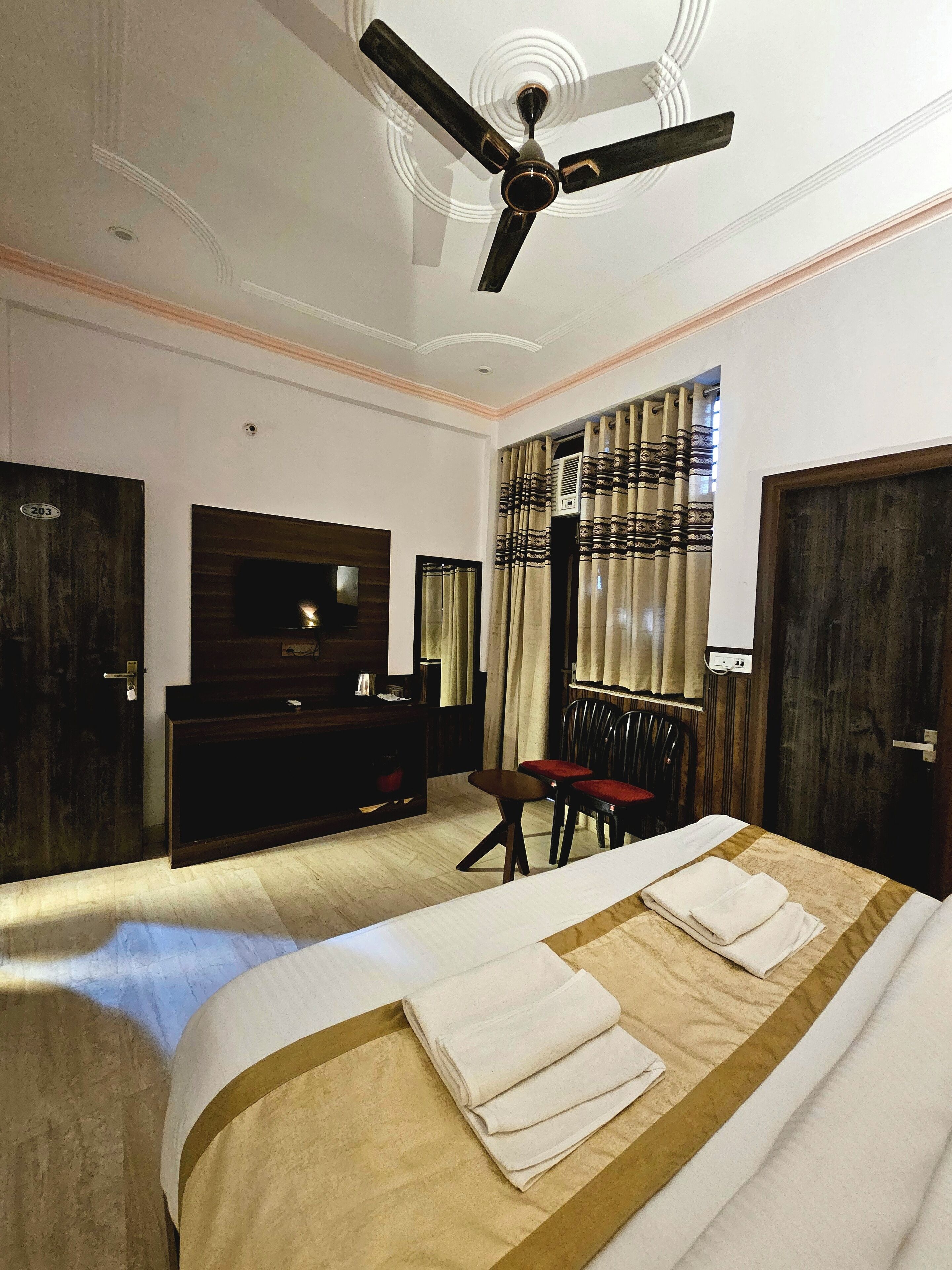 Une chambre d’hôtel équipée d’un lit, d’une télévision, d’un bureau, d’une chaise et d’un ventilateur de plafond.