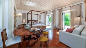 Een ruime slaapkamer met een groot bed, een zithoek met een bank en stoelen, een eettafel en uitzicht op groen.