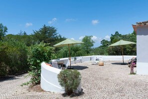 An outdoor patio with stone flooring, white walls, and green umbrellas. - Pine Tree House in Azeit o (Setubal)