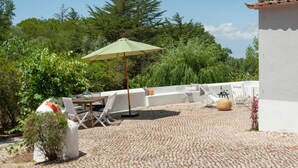 An outdoor patio with a table and chairs, a green umbrella, and a white wall. - Pine Tree House in Azeit o (Setubal)