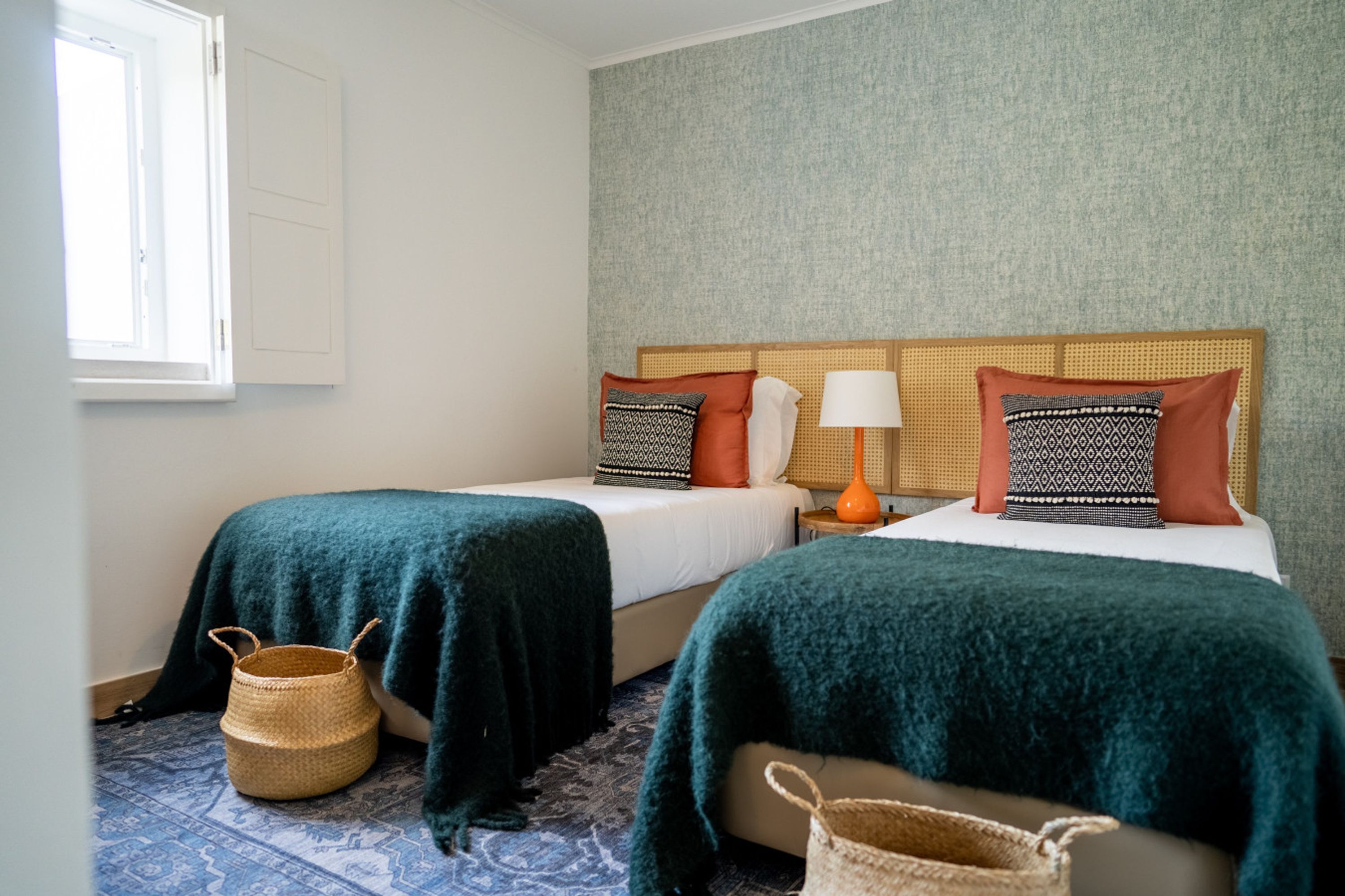 A hotel room with two beds, a window, a woven basket, and a patterned wall.
