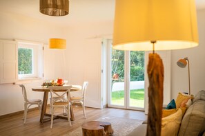 Un coin repas avec une table et des chaises en bois, une lampe jaune et une vue sur un jardin, visible à travers des portes vitrées.