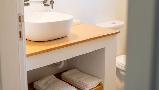 Un baño moderno con un lavamanos blanco, encimera de madera y un inodoro.