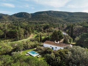 En villa med en swimmingpool, omgiven av frodig grönska och berg.