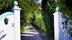A cobblestone pathway leading through a lush, green area with white and blue gates. - Wood Oven House II in Azeit o (Setubal)