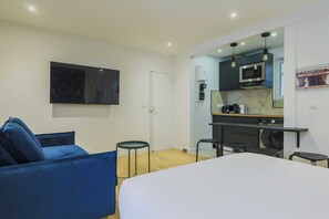 A modern hotel room with a bed, a blue sofa, a small round table, and a kitchenette with a microwave and coffee maker. - Modern Studio - 4P- Sacre-coeur (Paris)
