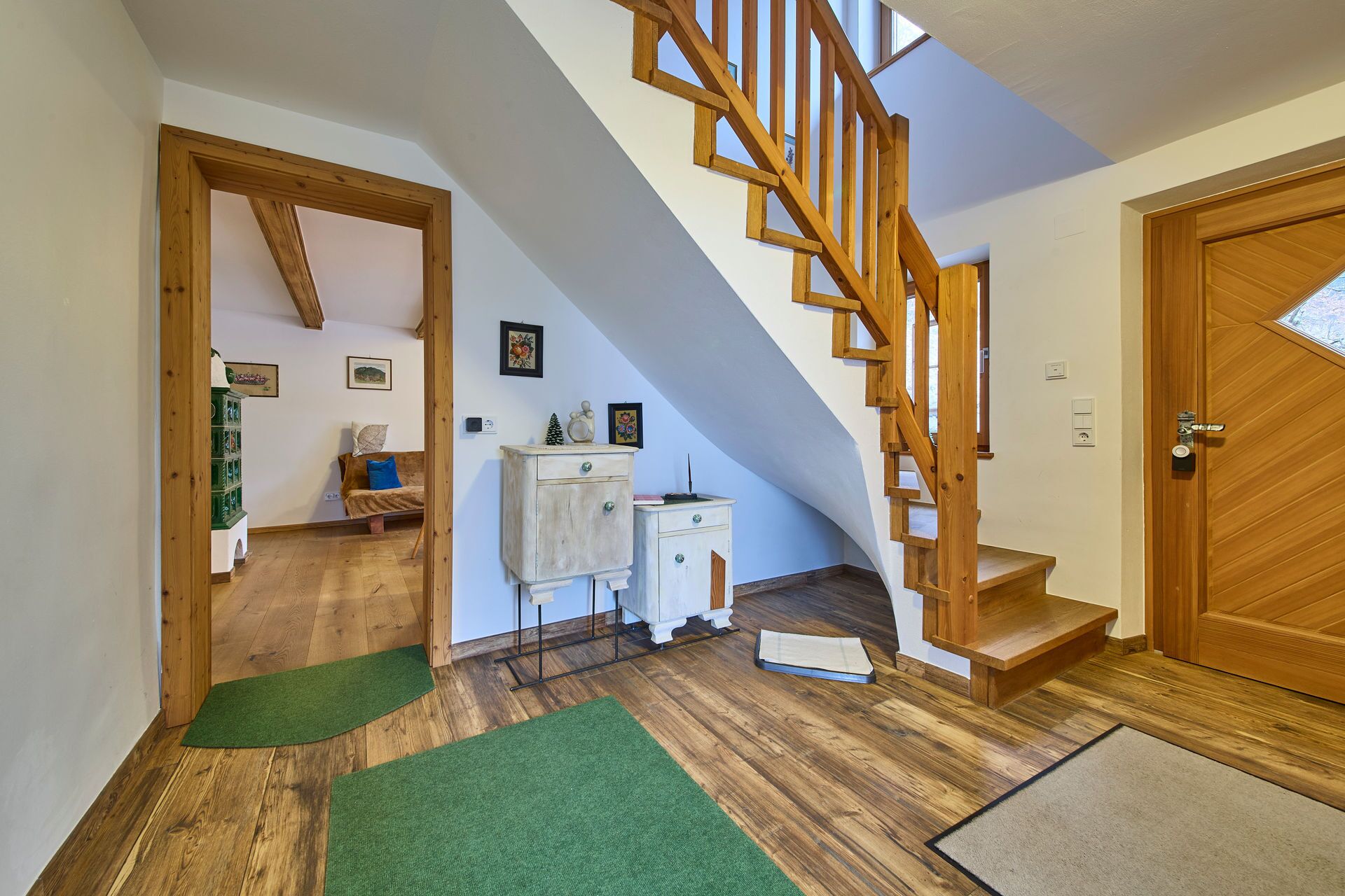 A wooden staircase leading to an upper floor, a white door, and a green mat at the entrance.