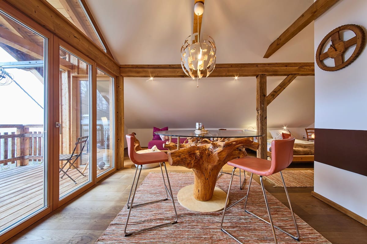 Un espace repas avec une table en bois entourée de chaises, un lustre et une grande fenêtre.