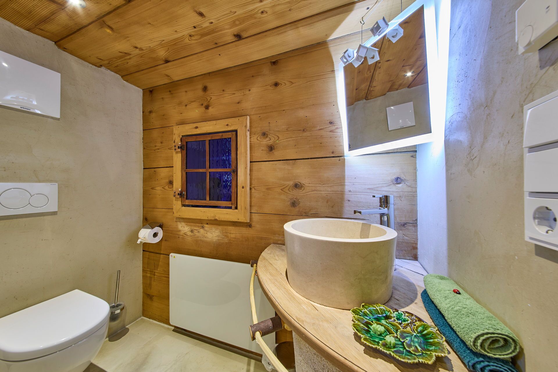 Ein Badezimmer mit Holzvertäfelung, Toilette, Waschbecken und Fenster.