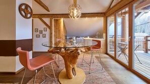 A dining area with a glass table centered on a tree stump base, surrounded by pink chairs. - Waldharmonie Chalet & Apartments (Bad Goisern)