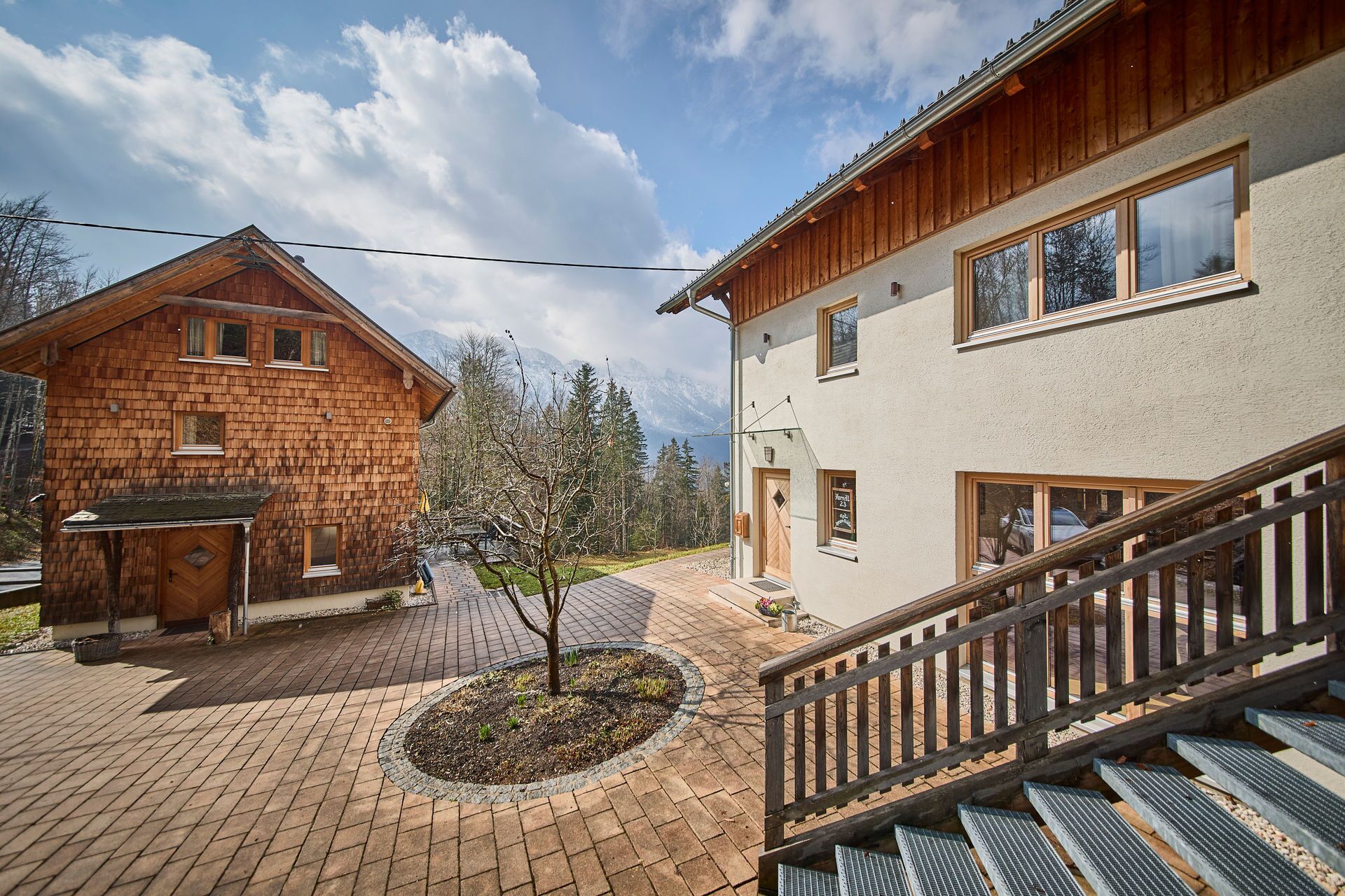 Un edificio a due piani con rivestimento in legno e facciata bianca, caratterizzato da un piccolo giardino e una scala che conduce al piano superiore.