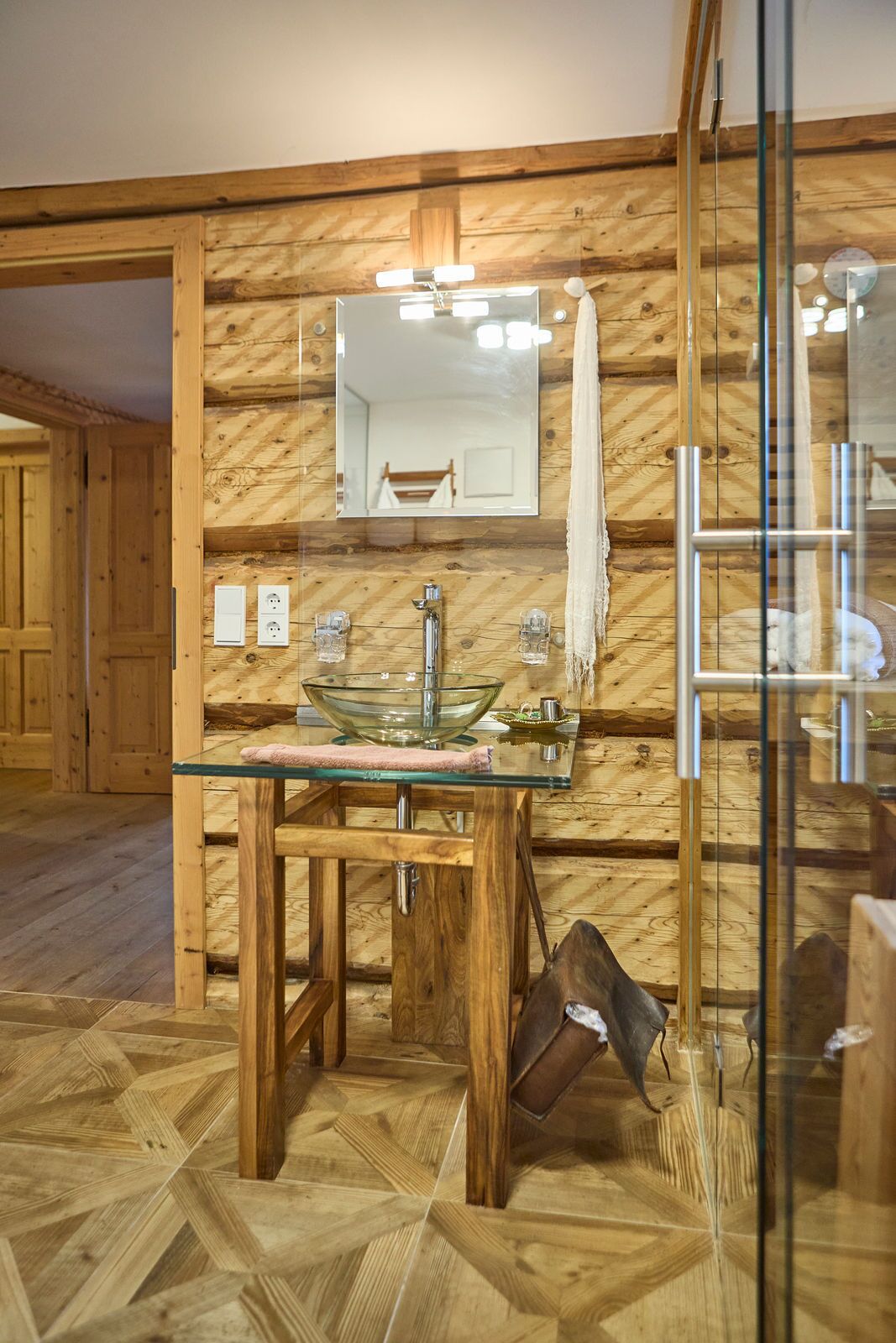 A wooden interior with a glass-top sink, a mirror, and a towel rack.