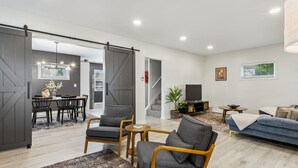 A modern living room with a dining area, a sofa, and a TV. There is a staircase leading to another level. - Stylish 3BR in Cleveland Hts |  Close to Clinic, UH (Cleveland Heights)