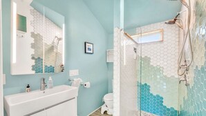 Une salle de bain avec un meuble-lavabo blanc, un miroir, des toilettes et un espace douche doté d’une porte en verre.