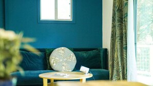 A room with a blue wall, a window, a sofa, a round table, and a potted plant. - Sky-High Treehouse | Pool & Hot Tub! (Austin)
