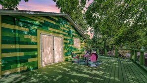 A green wooden deck with a covered seating area and a door. - Sky-High Treehouse | Pool & Hot Tub! (Austin)