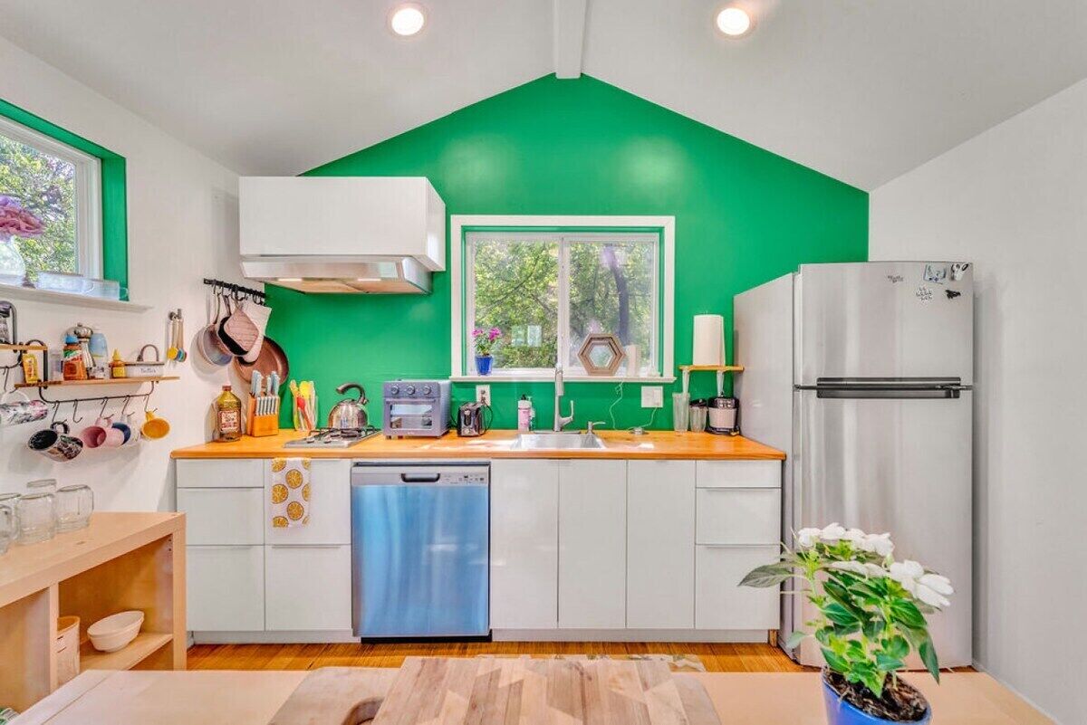 A kitchen with white cabinets, a green wall, a window, a sink, a dishwasher, and a refrigerator.