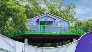 A single-story building with a green balcony, surrounded by trees. - The Hartyard | 3 Houses! | Pool & Hot Tub (Austin)