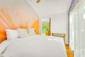 A bedroom with a large bed, a wooden headboard, a bedside table, and a view of the outdoors.