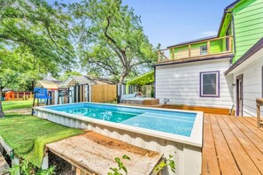 A residential property with a swimming pool, wooden deck, and a green house.
