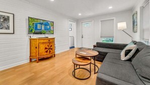 A living room with a sofa, a wooden cabinet, and a television on the wall. - The Hartyard | 3 Houses! | Pool & Hot Tub (Austin)