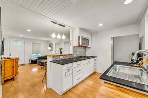 A modern kitchen with white cabinetry, a black countertop, and a stainless steel sink.
