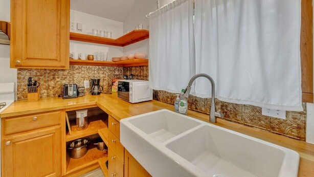 A compact kitchen with wooden cabinets, a double sink, and a microwave. - The Hartyard | 3 Houses! | Pool & Hot Tub (Austin)