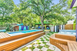 A backyard with a swimming pool, wooden deck seating, and a hot tub.