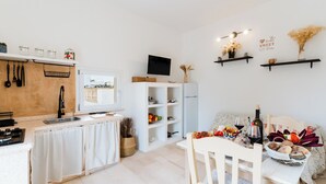 Une cuisine moderne avec un coin repas, des meubles blancs, un téléviseur et une table dressée avec de la nourriture et des boissons.